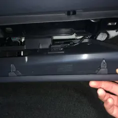 Dłoń otwiera schowek w Volvo V60, przygotowując do wymiany filtra kabinowego.