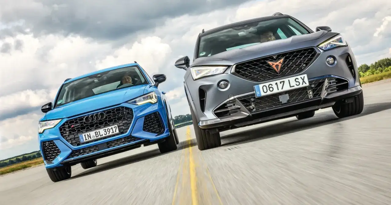 Dwa sportowe SUV-y, niebieski Audi i szary Cupra, pędzą po drodze.